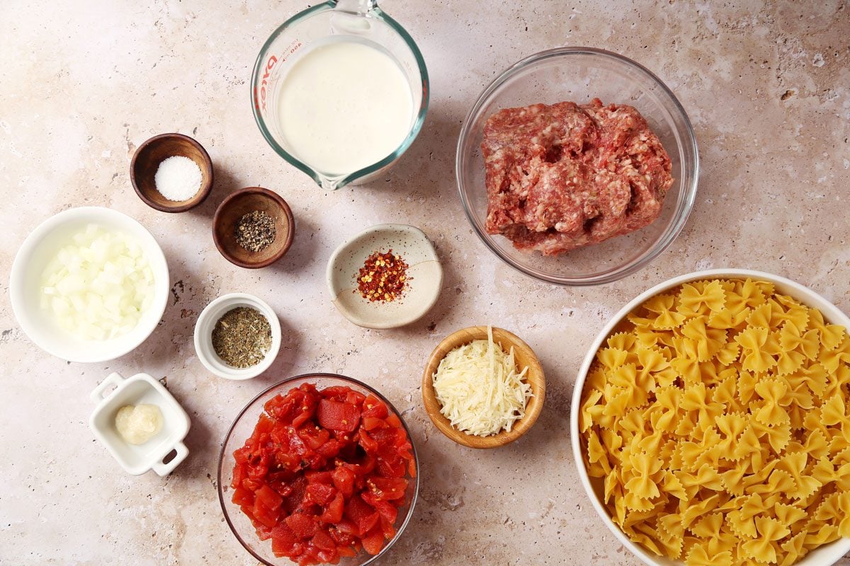 Ingredients for Taste of Home's Sausage and Bow Tie Pasta laid out in small bowls on a brown marble surface.