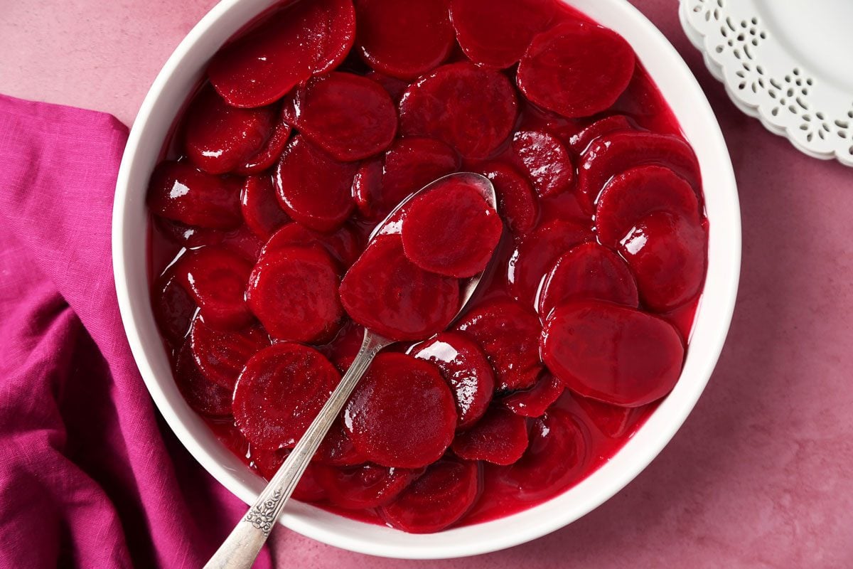 Close up of Taste of Home's Harvard Beets served on white plates on a magenta surface.