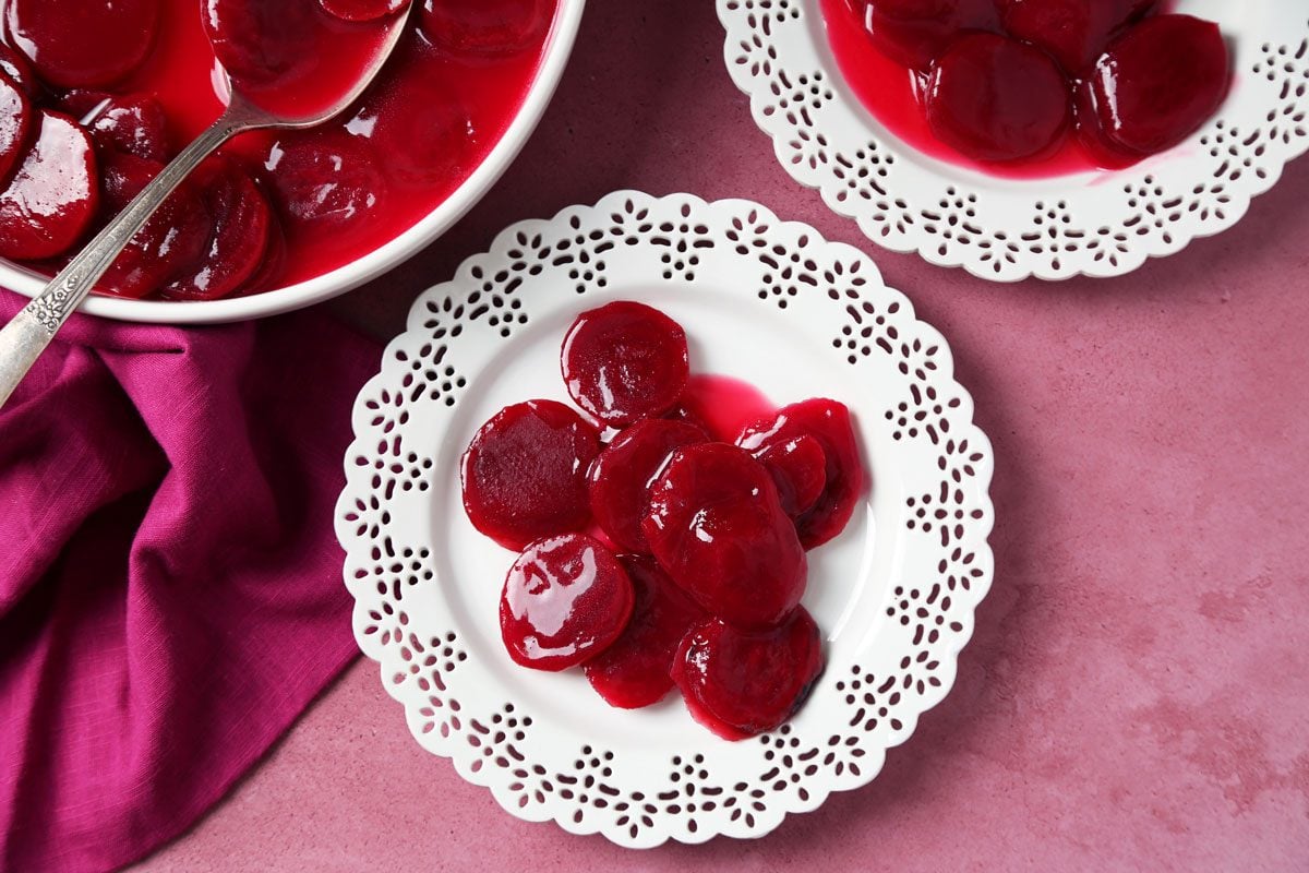 Close up of Taste of Home's Harvard Beets served on white plates on a magenta surface.