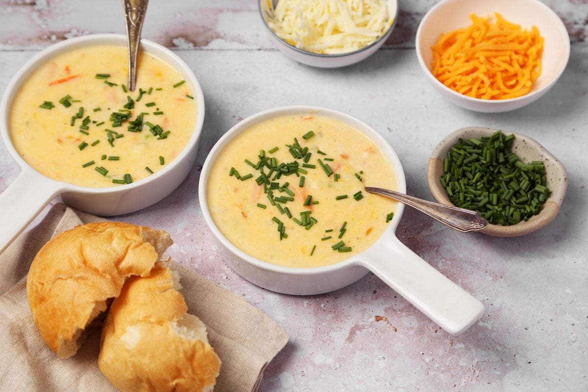 Close up of Taste of Home's Cheddar Cheese Soup served in soup bowls on a grey surface.