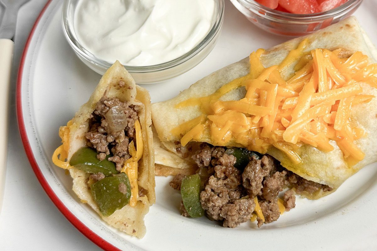 Taste of Home Taco Burrito on an enamel plate with bowls of sour cream and tomatoes