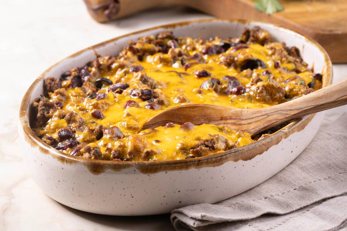 Tamale Casserole in dish with cutting board in the background at 3/4 view on marble