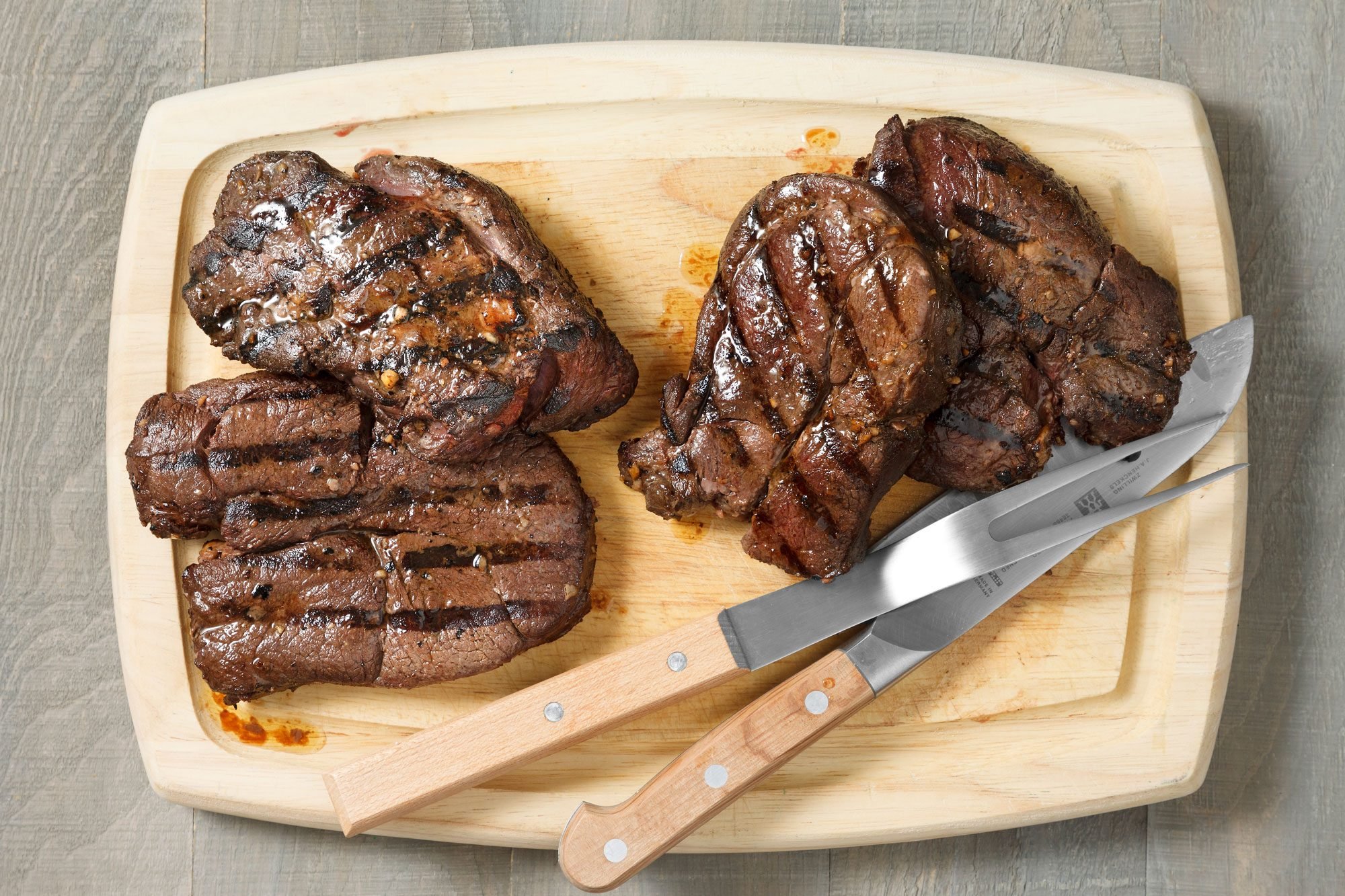 overhead shot of grilled venison steaks on a wooden board with knife