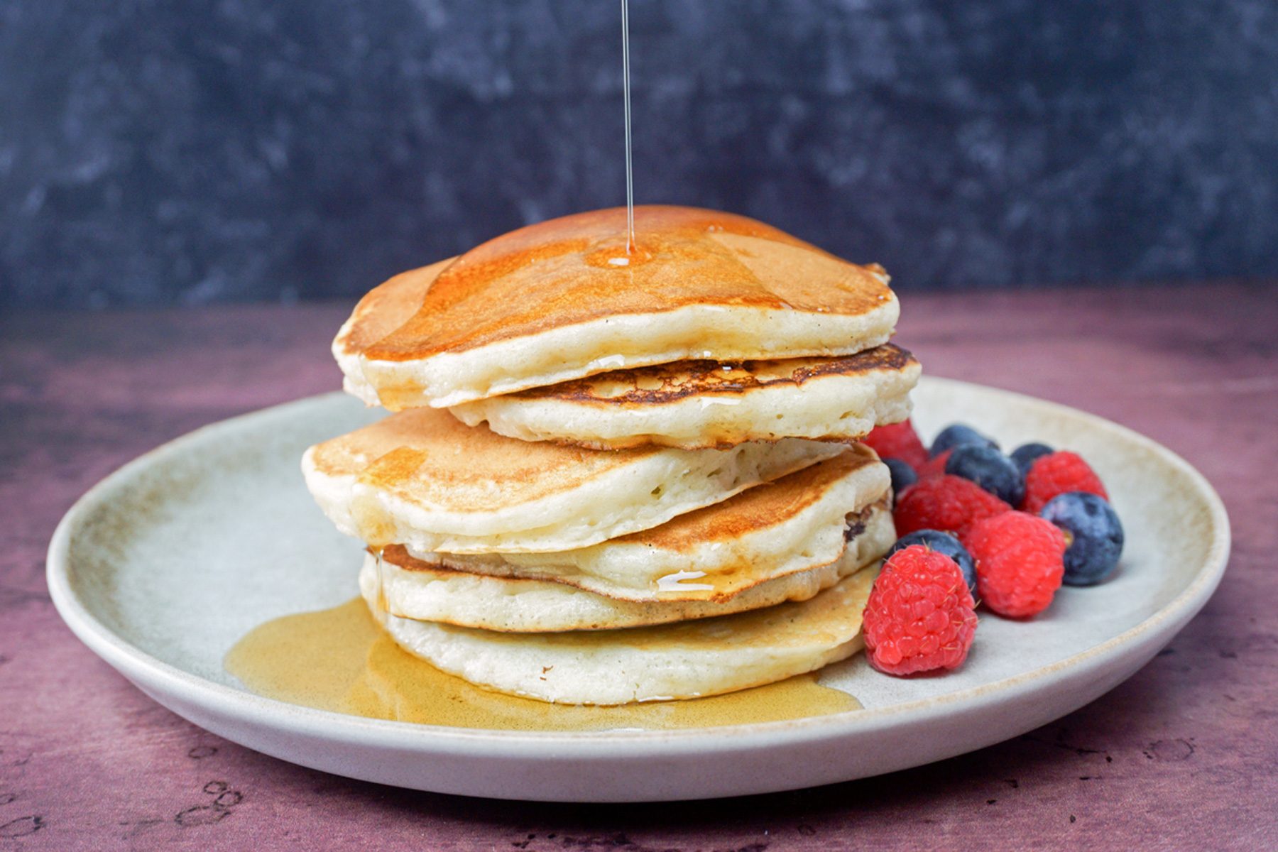 ice cream pancakes stacked with strawberries and blue berries on the side. honey being dripped from top