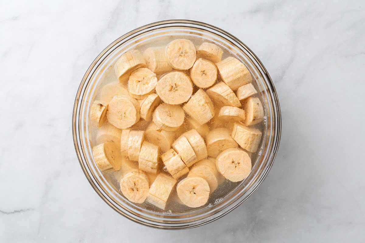 Chopped and peeled plantains soaking in seasoned water in a mixing bowl for step one of Air-Fryer Plantains recipe for Taste of Home