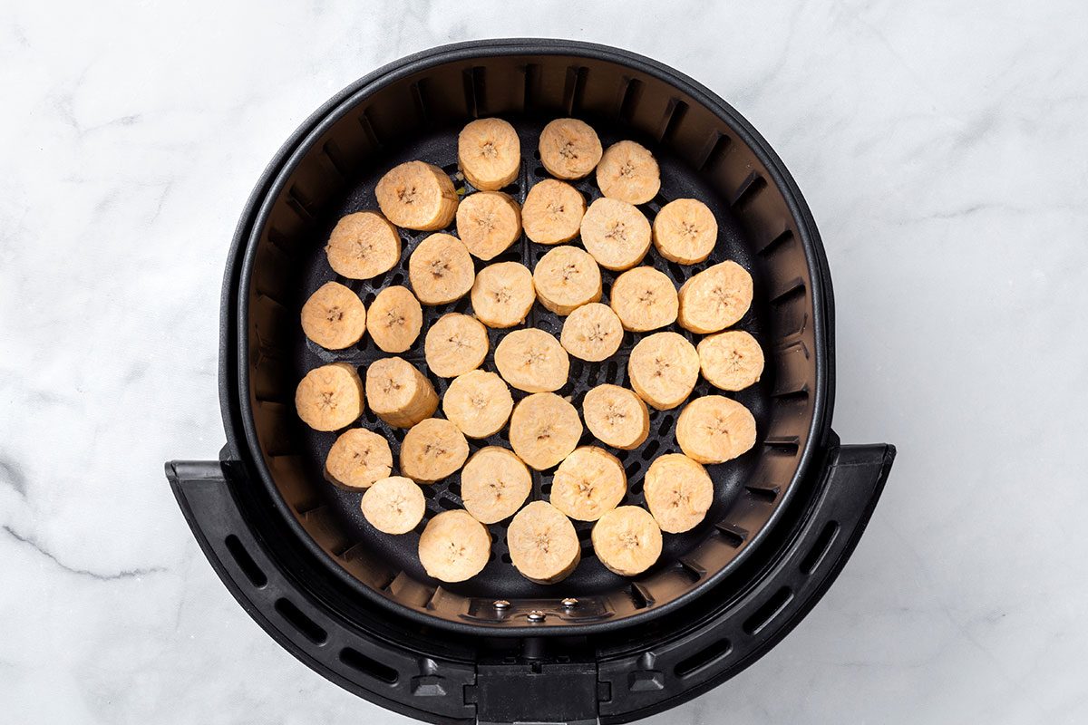Plantain slices in an air fryer basket for step two of Air-Fryer Plantains recipe for Taste of Home