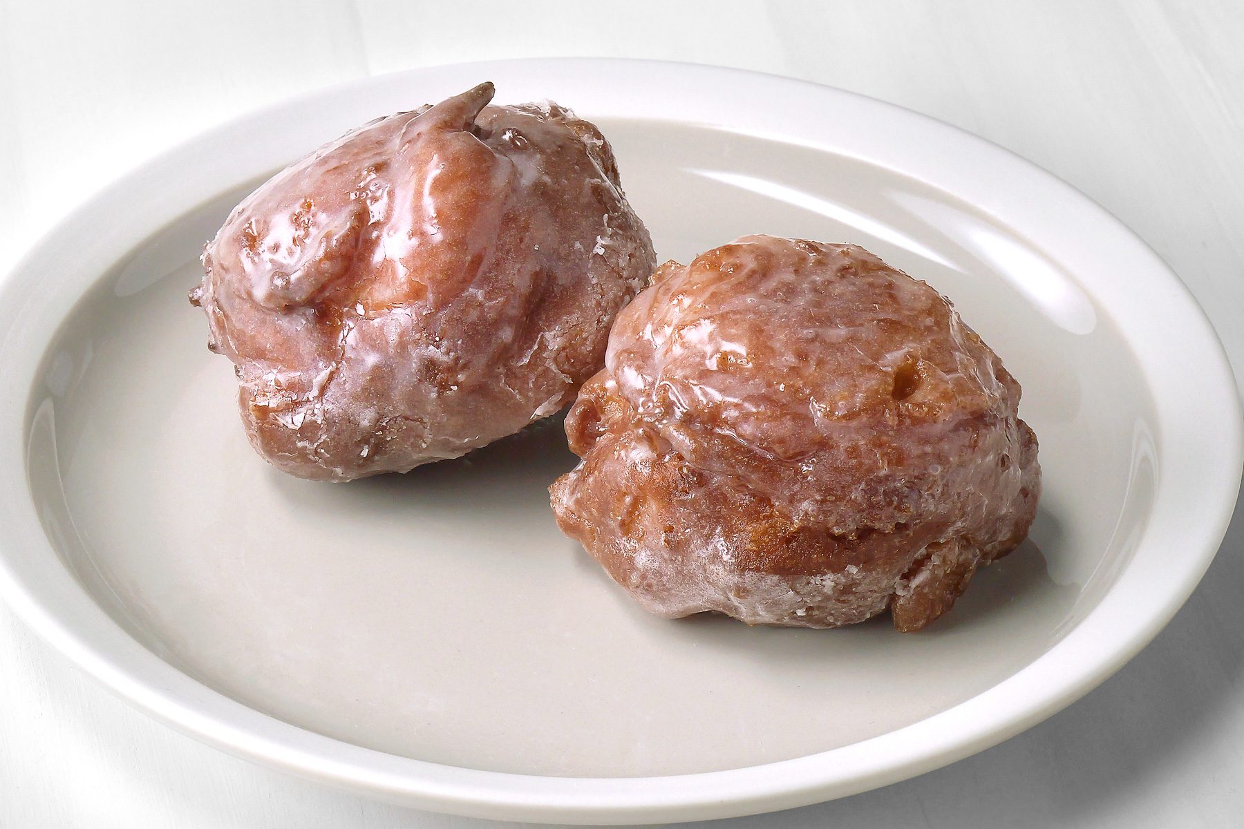 overhead shot of a white plate filled with two Apple Fritters; the plate is sitting on a white marble surface