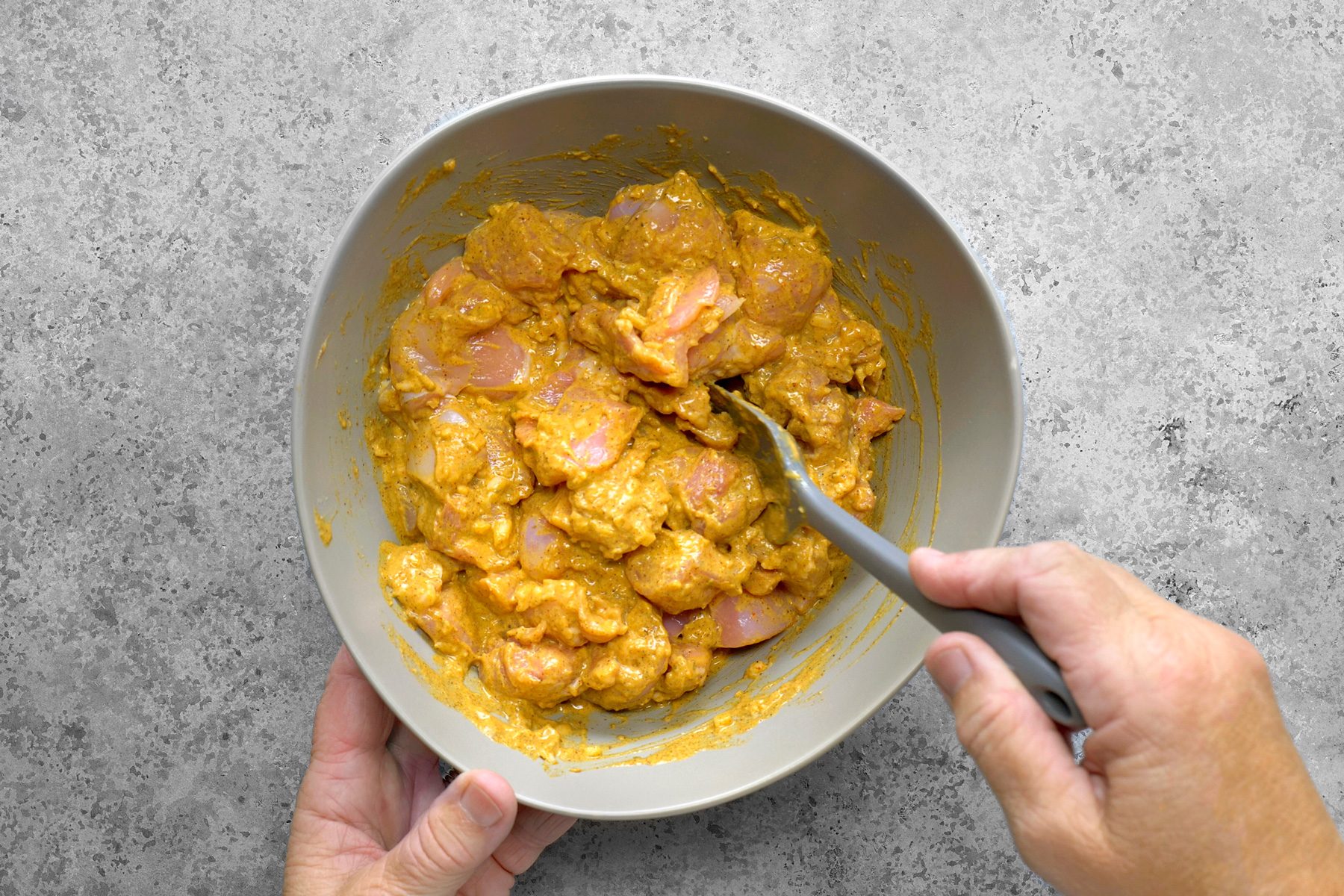 A person is marinating chicken pieces in a bowl, gently coating each piece with a rich blend of spices and sauces.