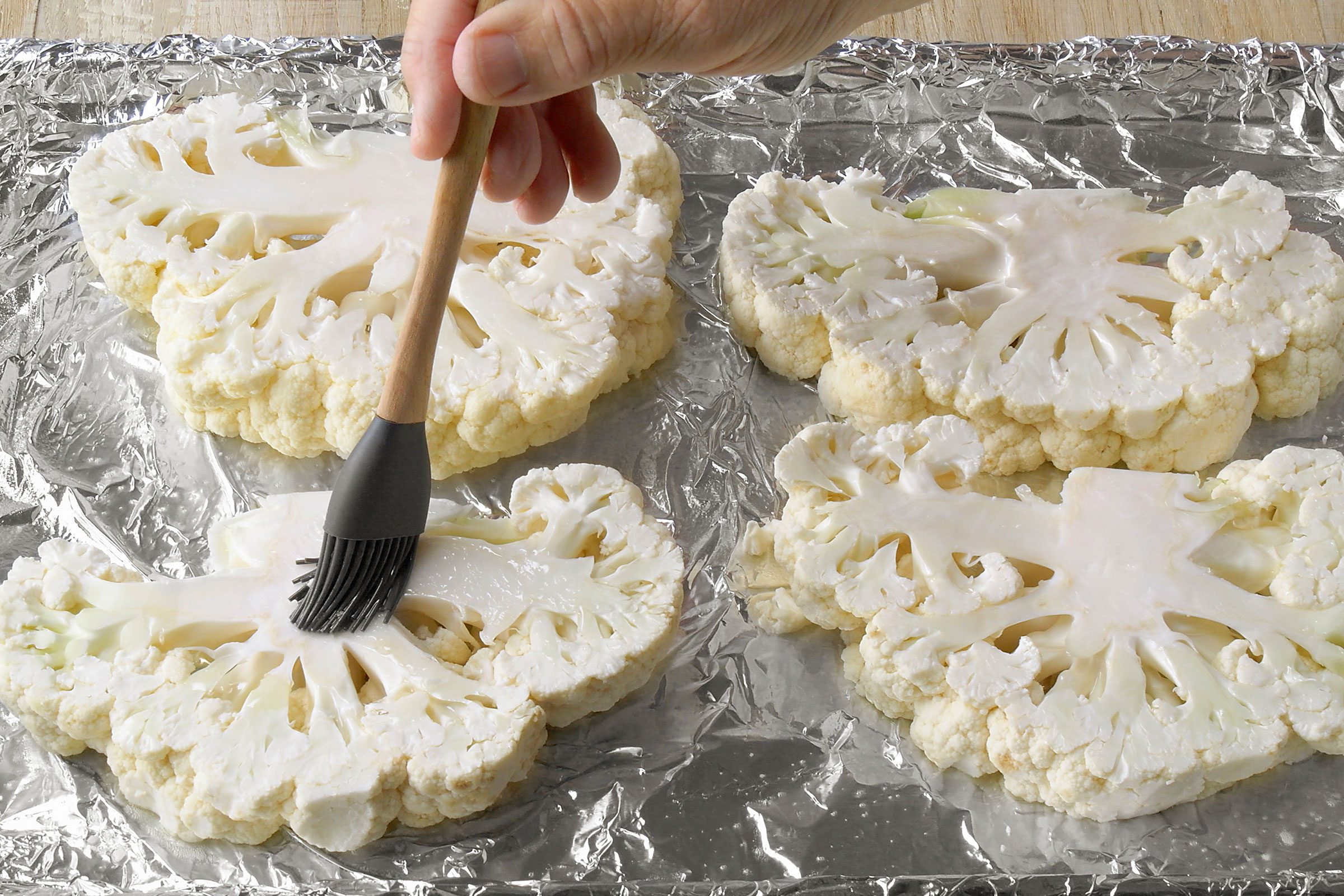 Brushing cauliflower slices with olive oil