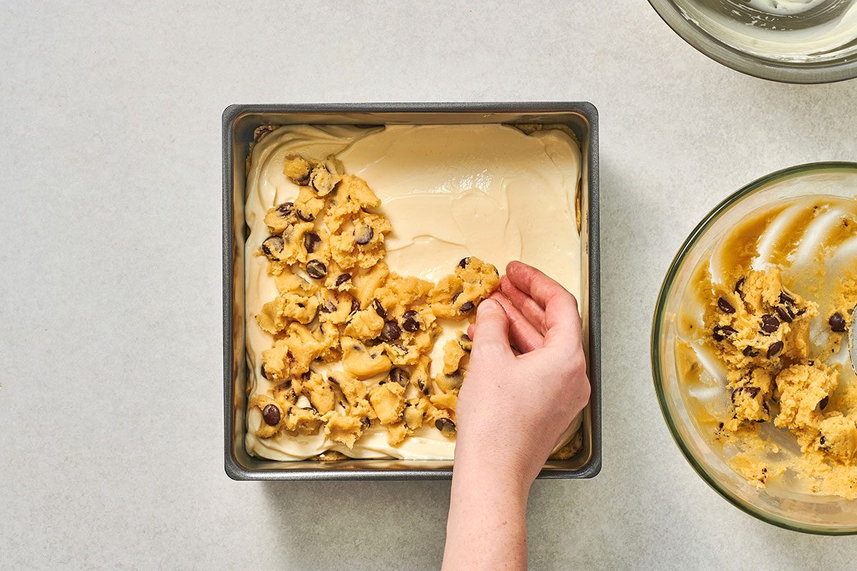 Half of the cookie dough pressed into the bottom of a square baking pan
