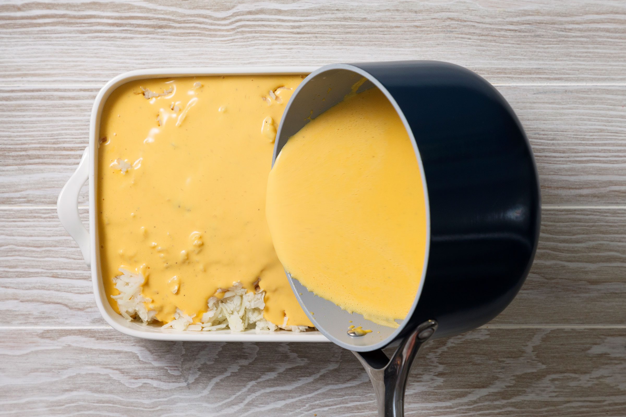 Pouring of cheese sauce on shredded potatoes