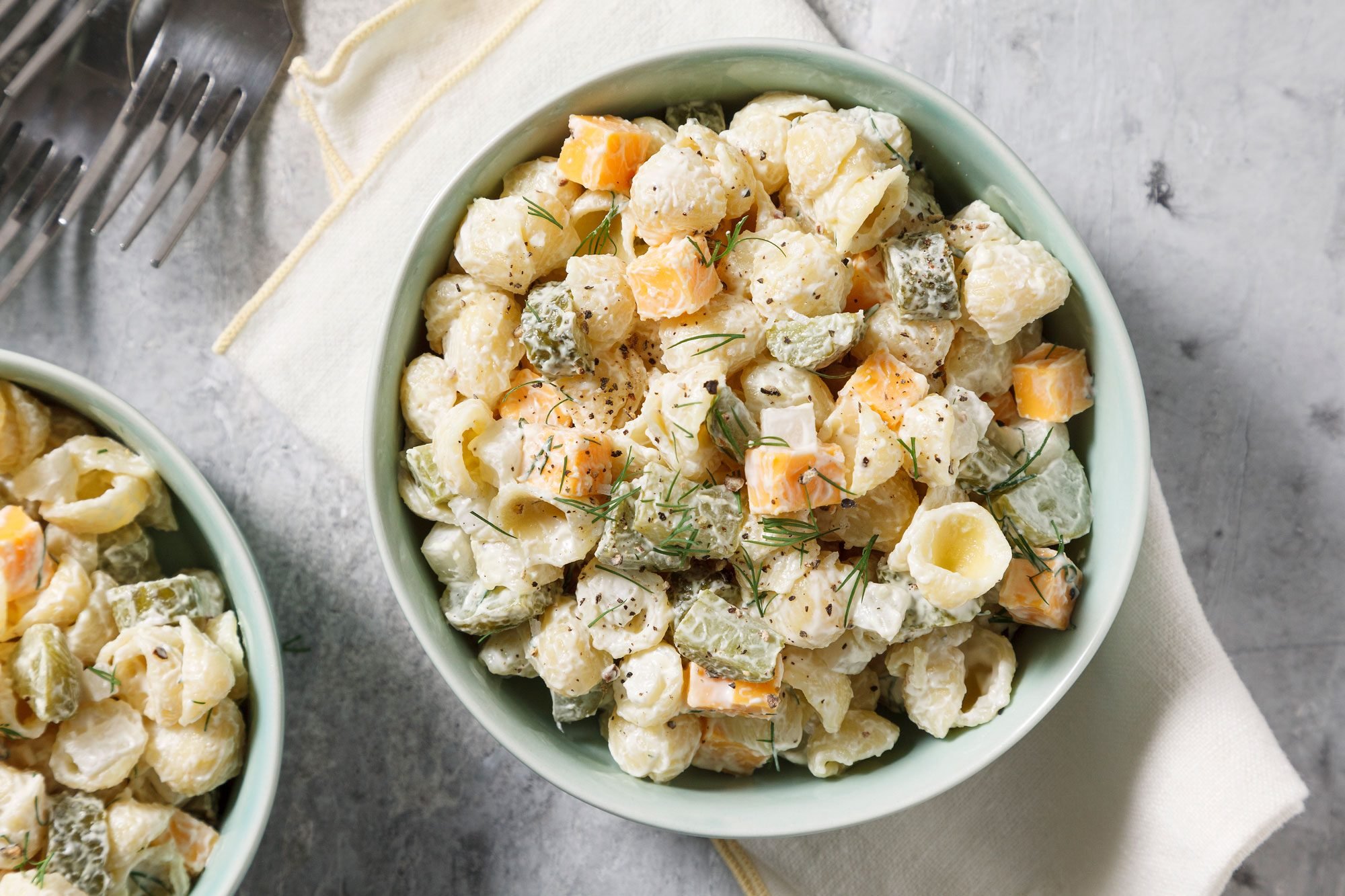 Top view shot of Dill Pickle Pasta Salad; serve in bowls; forks; napkin; grey surface;