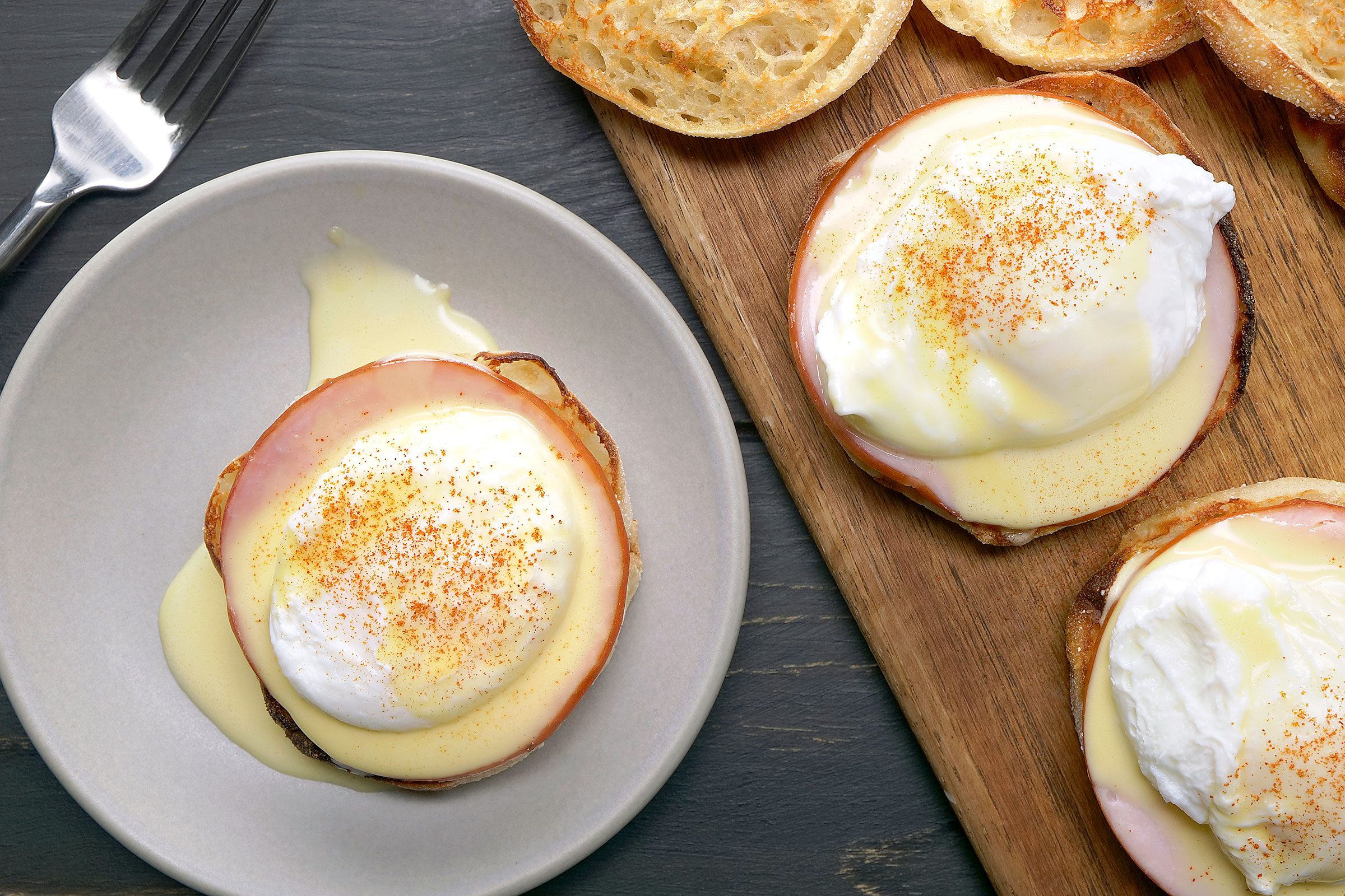 Eggs Benedict served in a white plate and some on a wooden board
