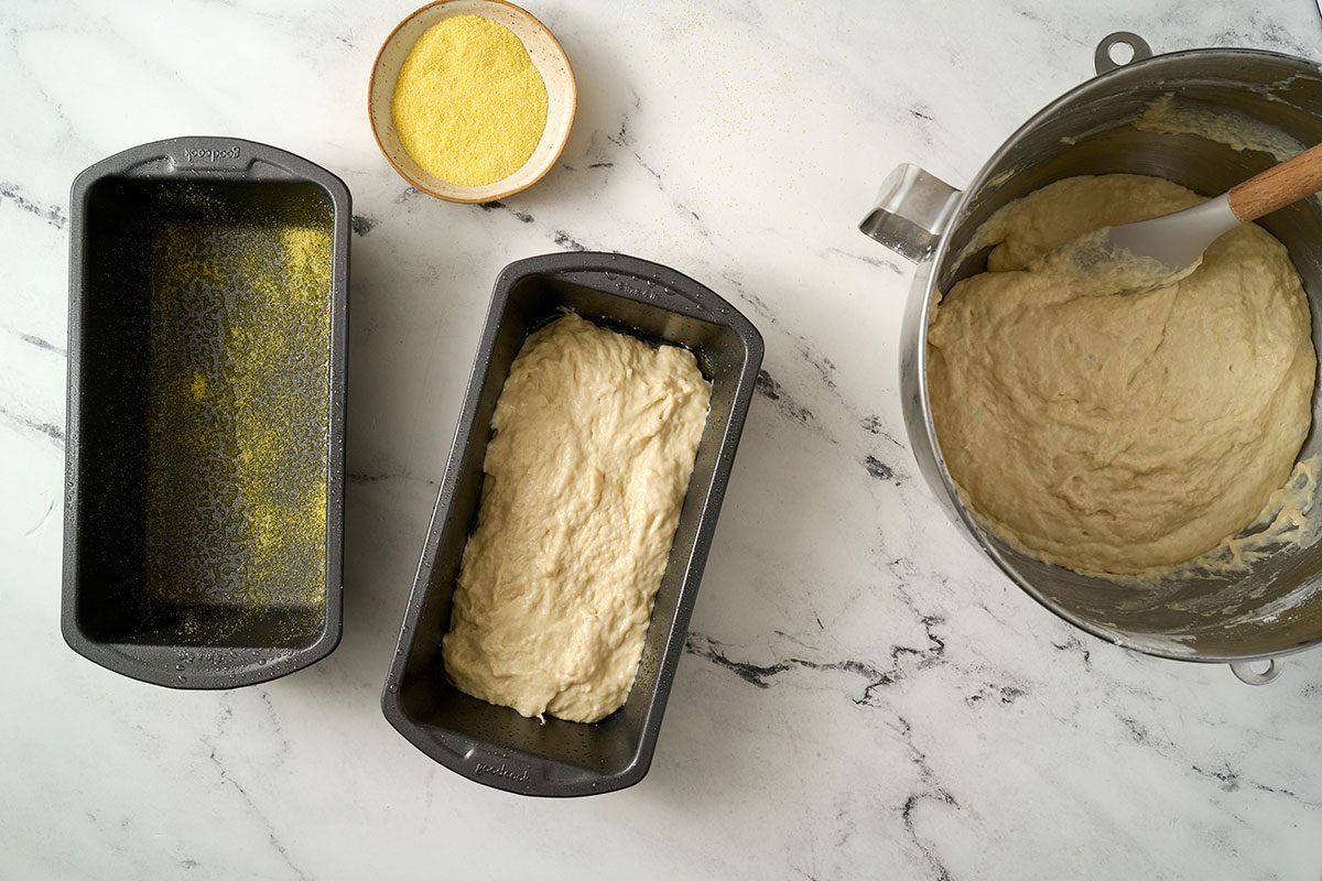 Overhead view of the stiff batter spread in two greased loaf pans, sprinkled with cornmeal on top, and covered to rise for the Taste of Home English Muffin Bread recipe.