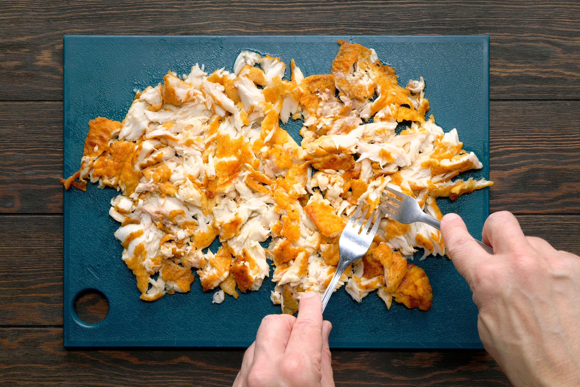 Flaking cooked fish into small chunks on a kitchen board