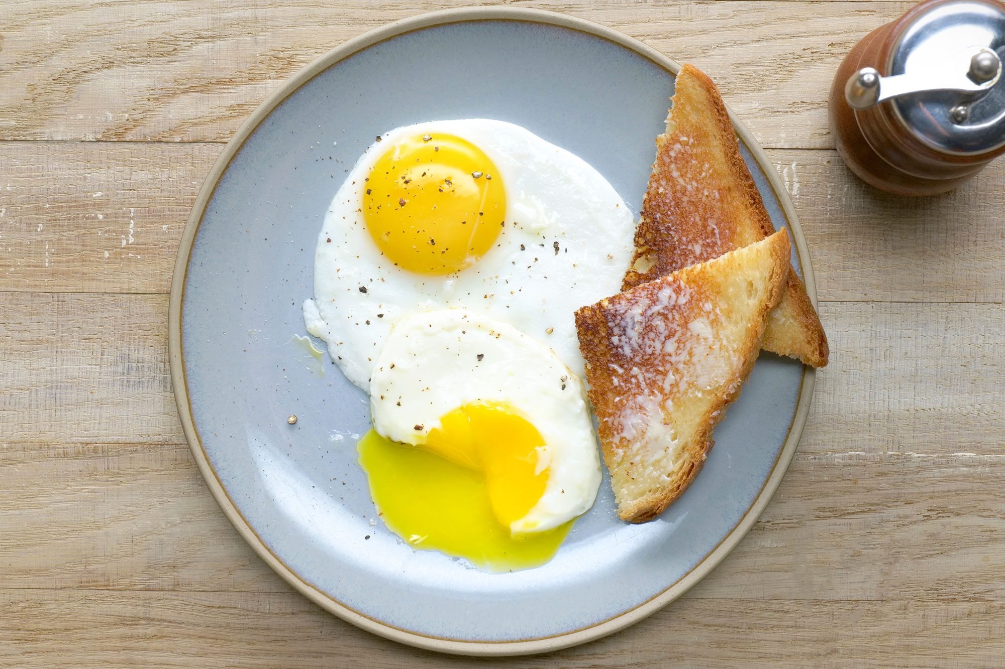 Overhead shot of Fried Eggs; serve on plate with bread toasts; wooden surface;