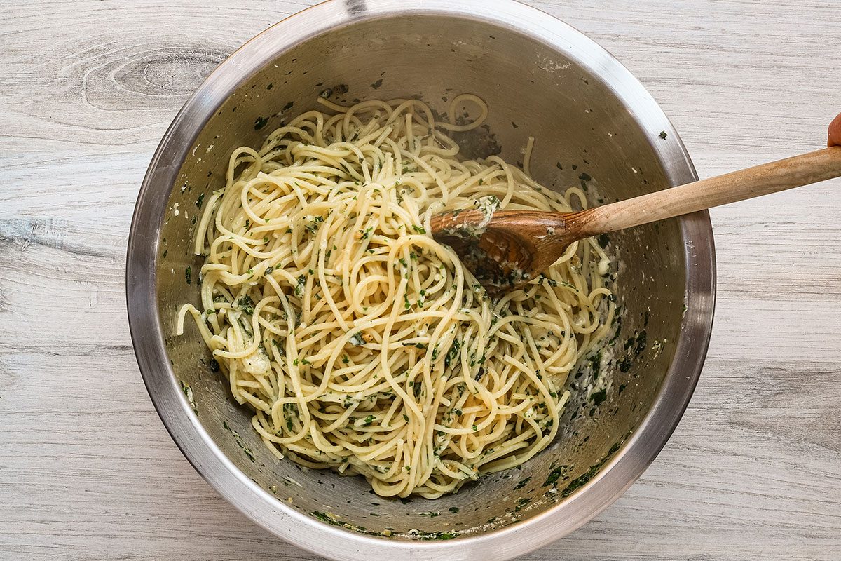 Garlic spaghetti preparation in a bowl with the garlic, herbs and seasonings combined with the pasta.