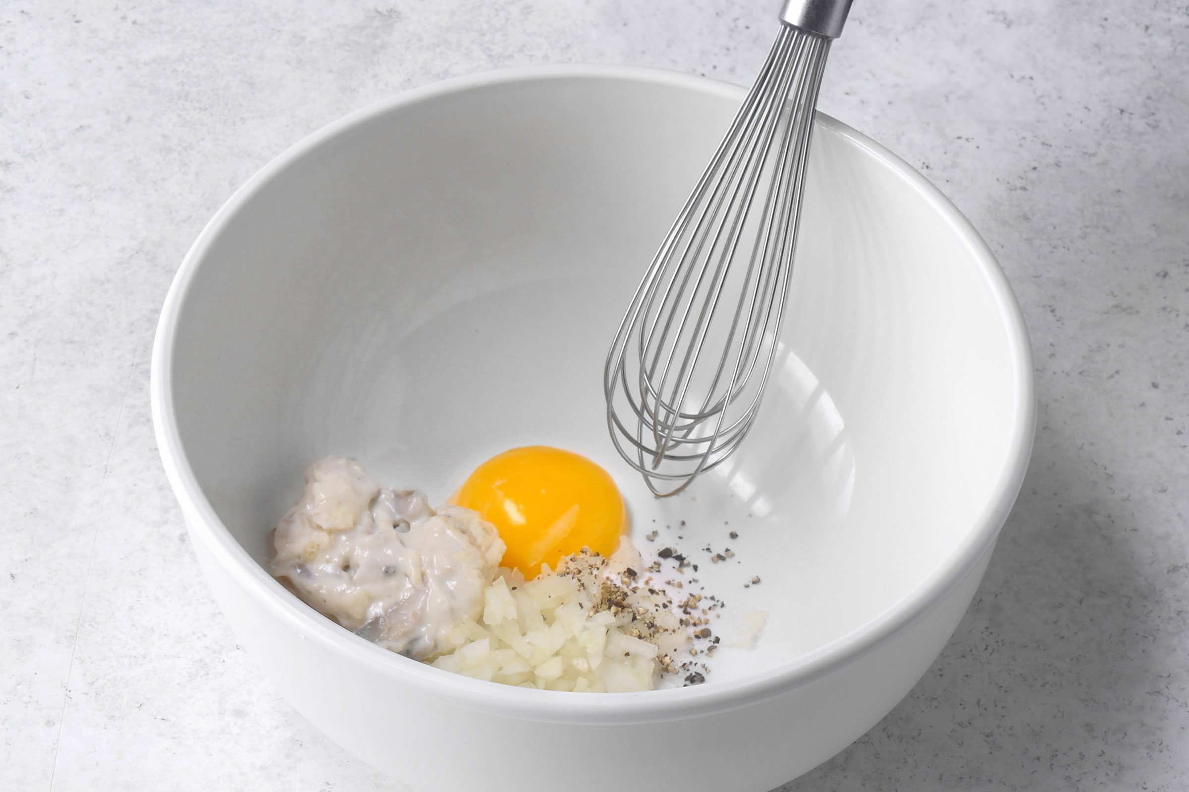 Egg yolk, pepper, mushroom sauce and chopped onions in a bowl with a whisker