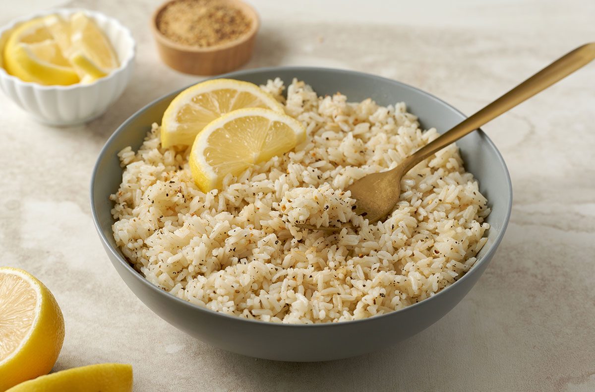 Close-up horizontal shot of Taste of Home Lemon Rice, showing the vibrant, fluffy texture of the rice, garnished with lemon zest and lemon-pepper seasoning.