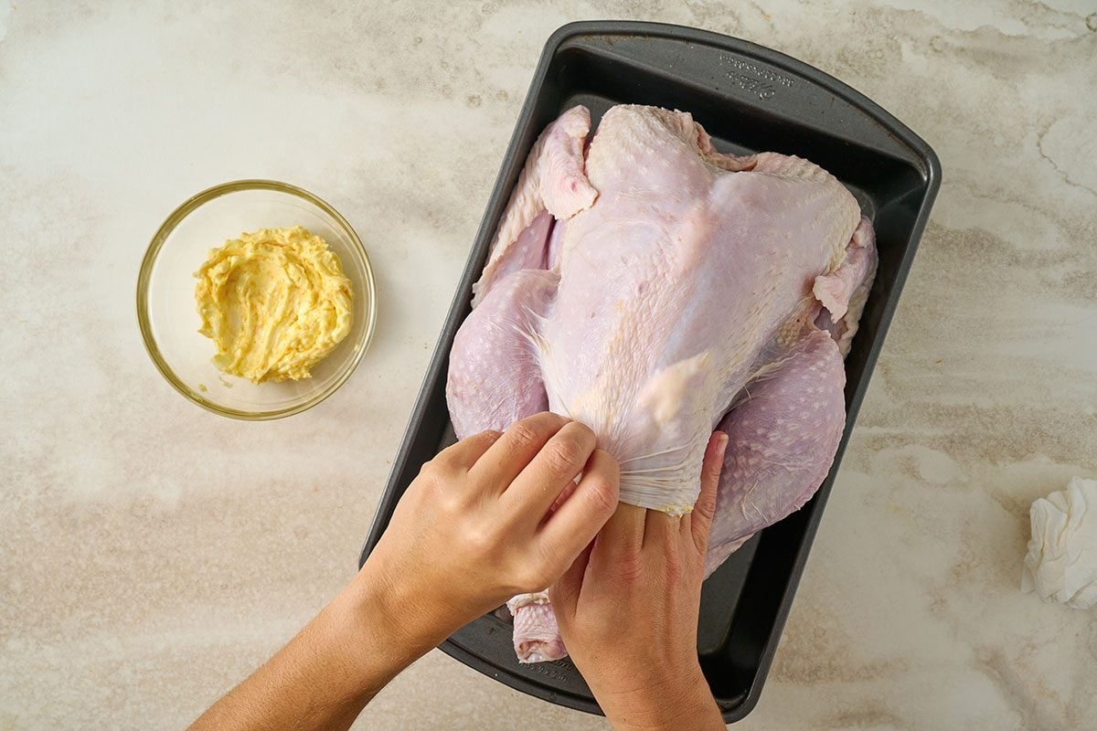 Overhead view of the butter and orange zest mixture being rubbed beneath the skin of the turkey, with the skin gently lifted to allow even distribution for the Taste of Home Orange Turkey recipe.