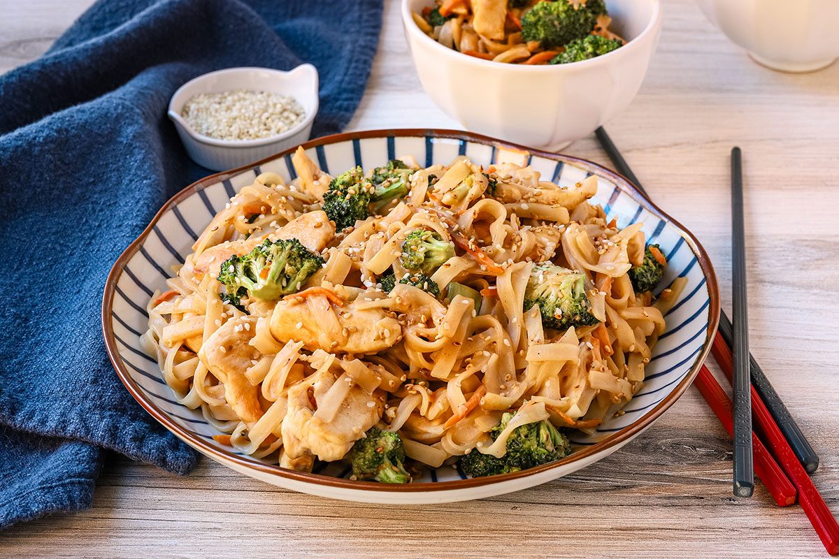 Peanut chicken stir fry in a bowl with broccoli, carrots, sesame seeds and a peanut sauce.