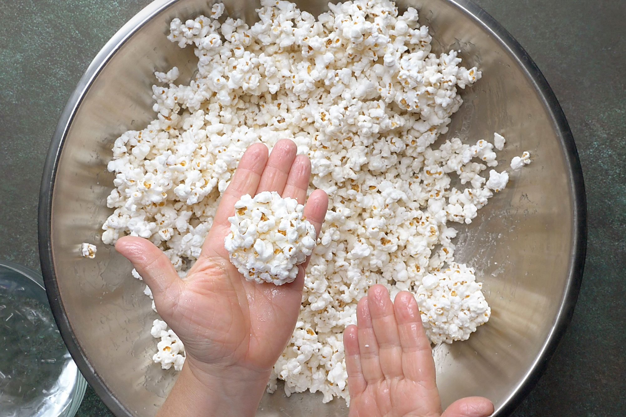 Overhead shot; when mixture is cool enough to handle quickly shape into balls; dipping hands into cold water as needed to prevent sticking; green marble surface;