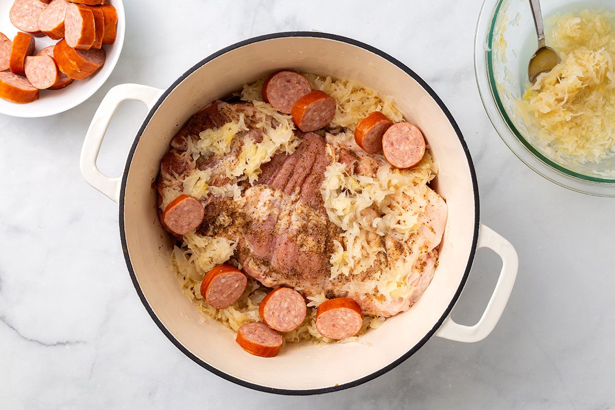 Seasoned pork loin roast in a Dutch Oven with sauerkraut and polish sausage for step four of Pork Roast and Sauerkraut recipe for Taste of Home
