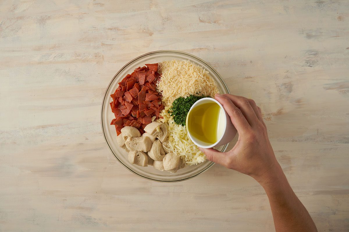 Overhead view of the dough, pepperoni, mozzarella, Parmesan, parsley flakes, olive oil, and minced garlic tossed together in a large bowl for the Taste of Home Pull Apart Pizza recipe.