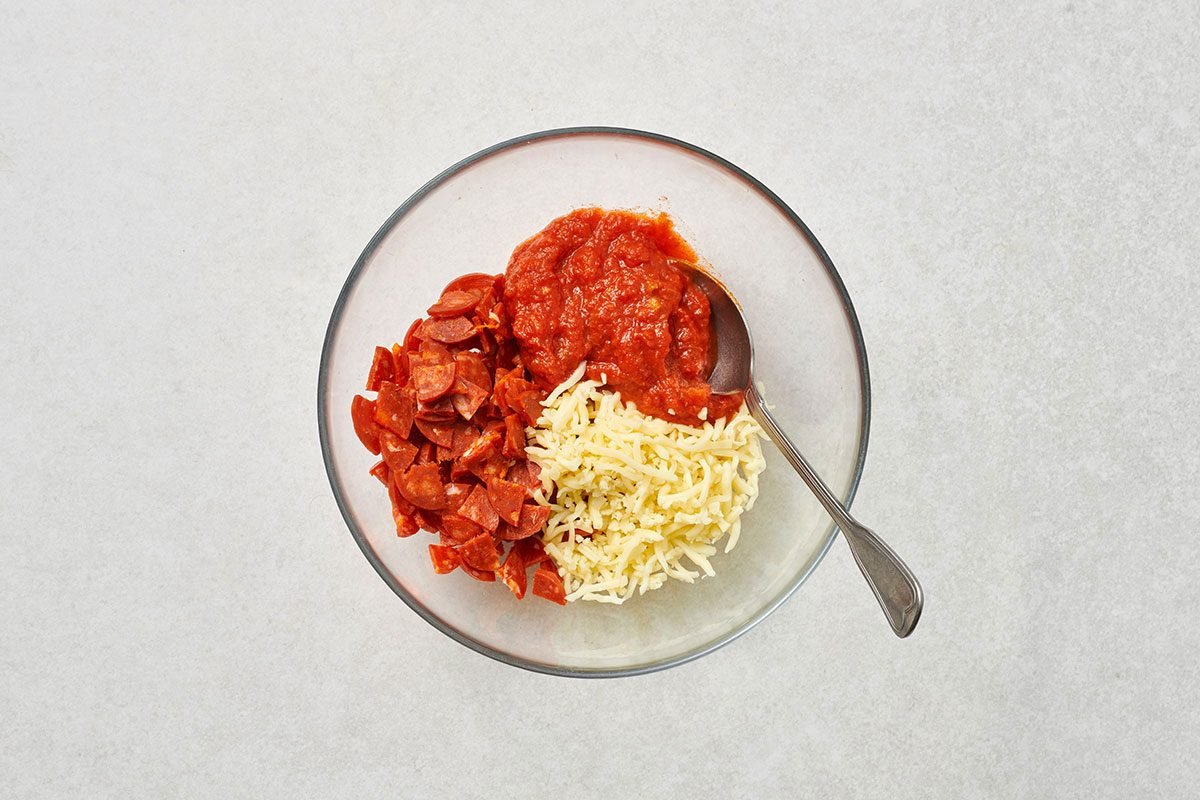 Chopped pepperoni, pasta sauce, and mozzarella combined in a small bowl 