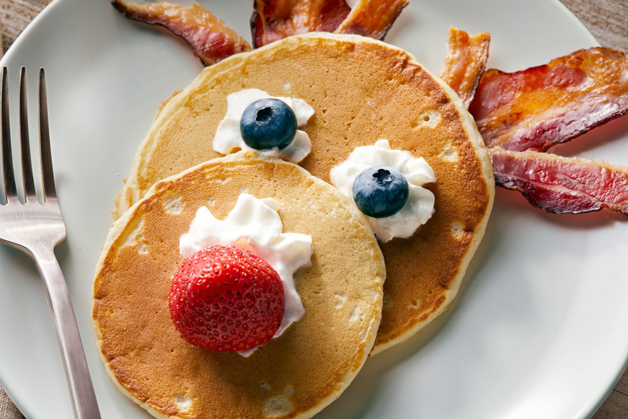 Close up shot of Reindeer Pancakes served in a plate with whipped cream, blueberries, strawberries, and beacon