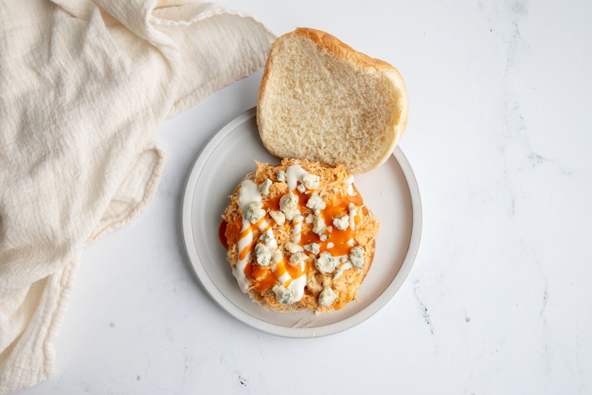 Beauty shot for Taste of Home Shredded Buffalo Chicken with mixture on a bun dressed with blue cheese and ranch dressing.
