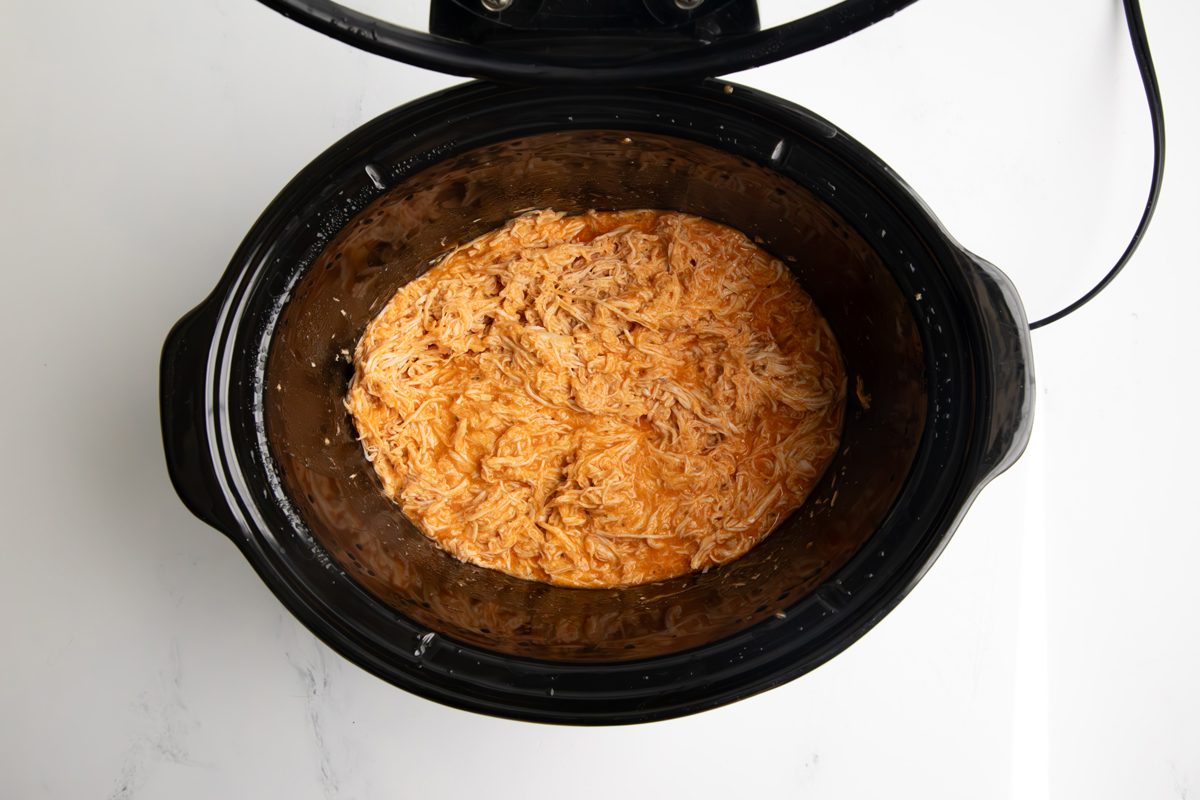 Overhead shot for Taste of Home Shredded Buffalo Chicken with chicken, buffalo sauce, and ranch seasoning in a large slow cooker after being shredded.