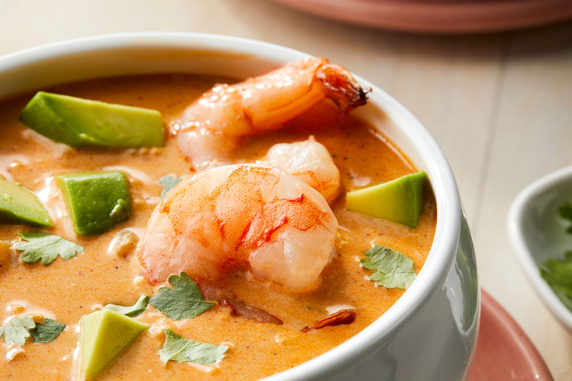 Close-up shot of Shrimp Bisque served in a bowl garnished with cilantro, avocado and additional shrimp