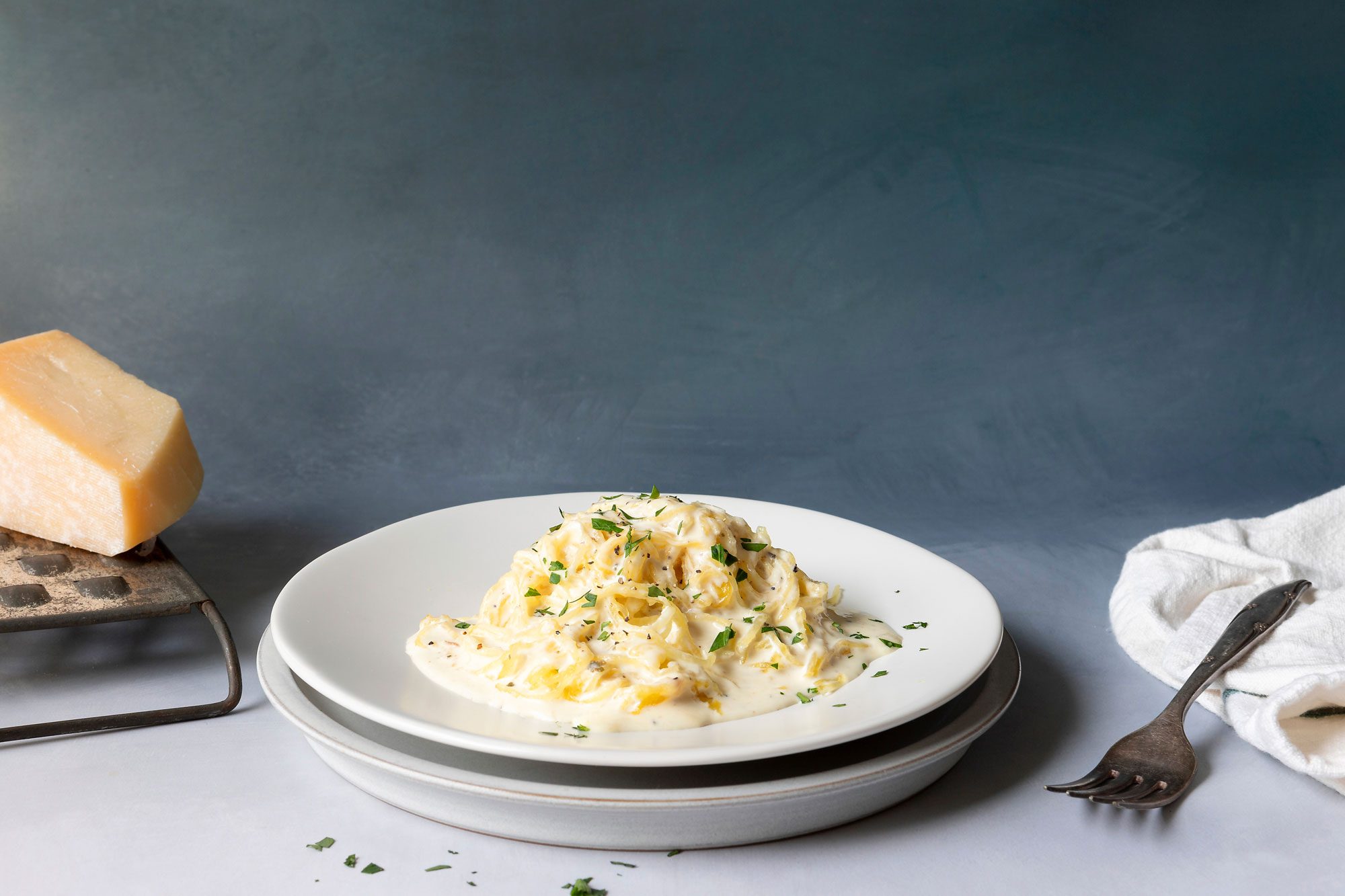 Spaghetti Squash Alfredo served in a bowl with fresh parsley on top and parmesan cheese on the side