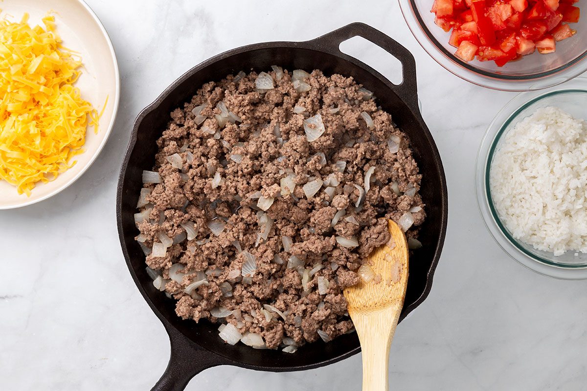 Ground beef and onion cooking in a cast iron skillet for step two of Stuffed Peppers with Cheese recipe for Taste of Home