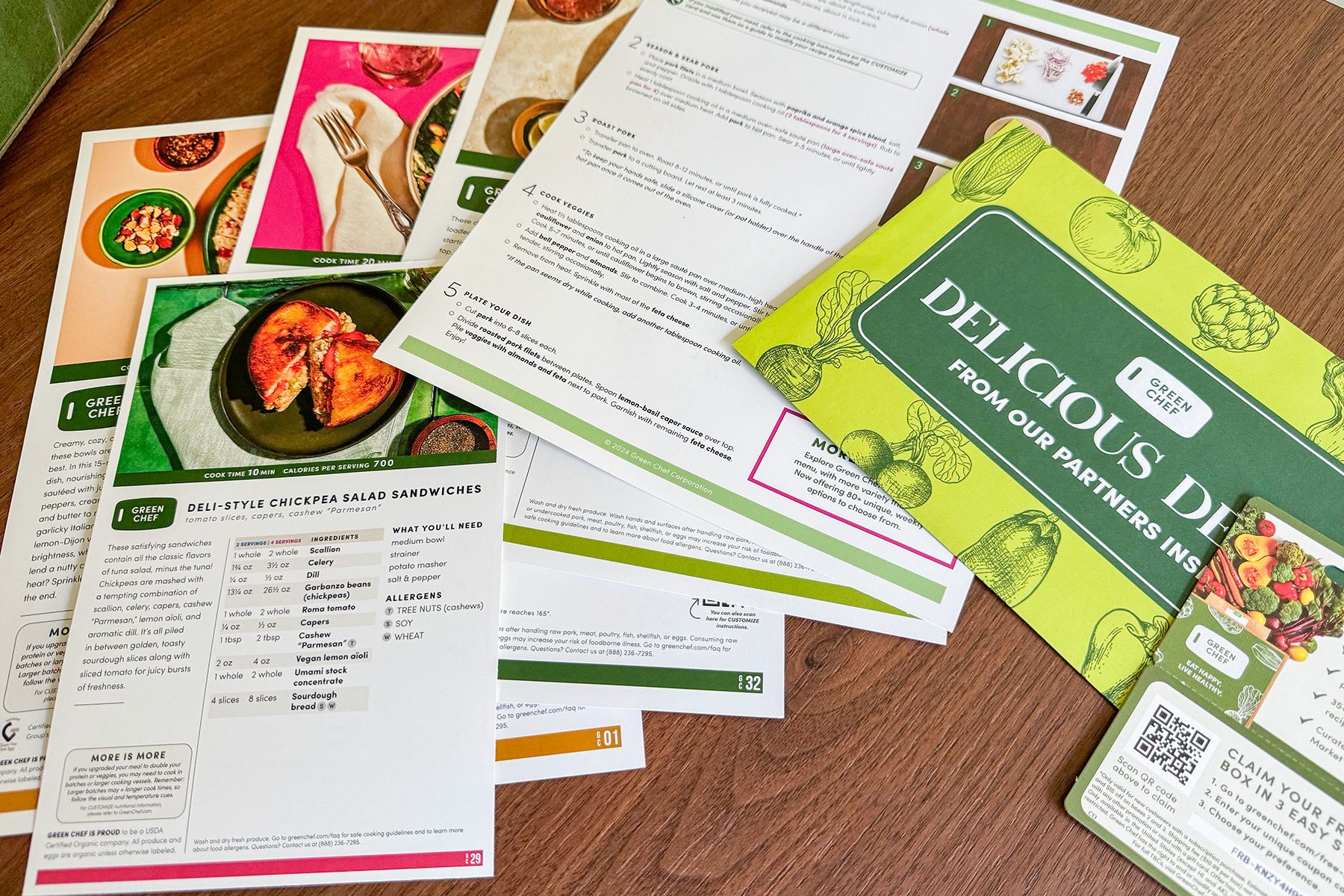 Scattered recipe cards and a "Delicious Deals" pamphlet are spread on a wooden surface. The cards feature images of meals, ingredients, and cooking instructions.