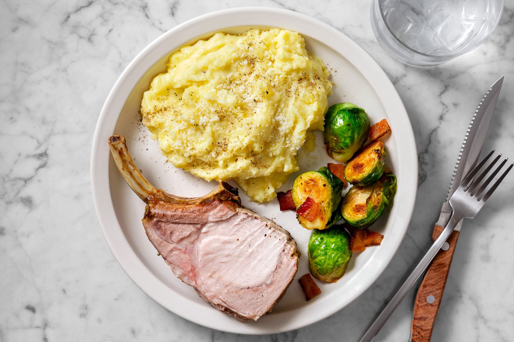 Overhead shot of Truffle Mashed Potatoes; serve on plate with rib and optional veggies; knife and fork; a glass water; marble surface;