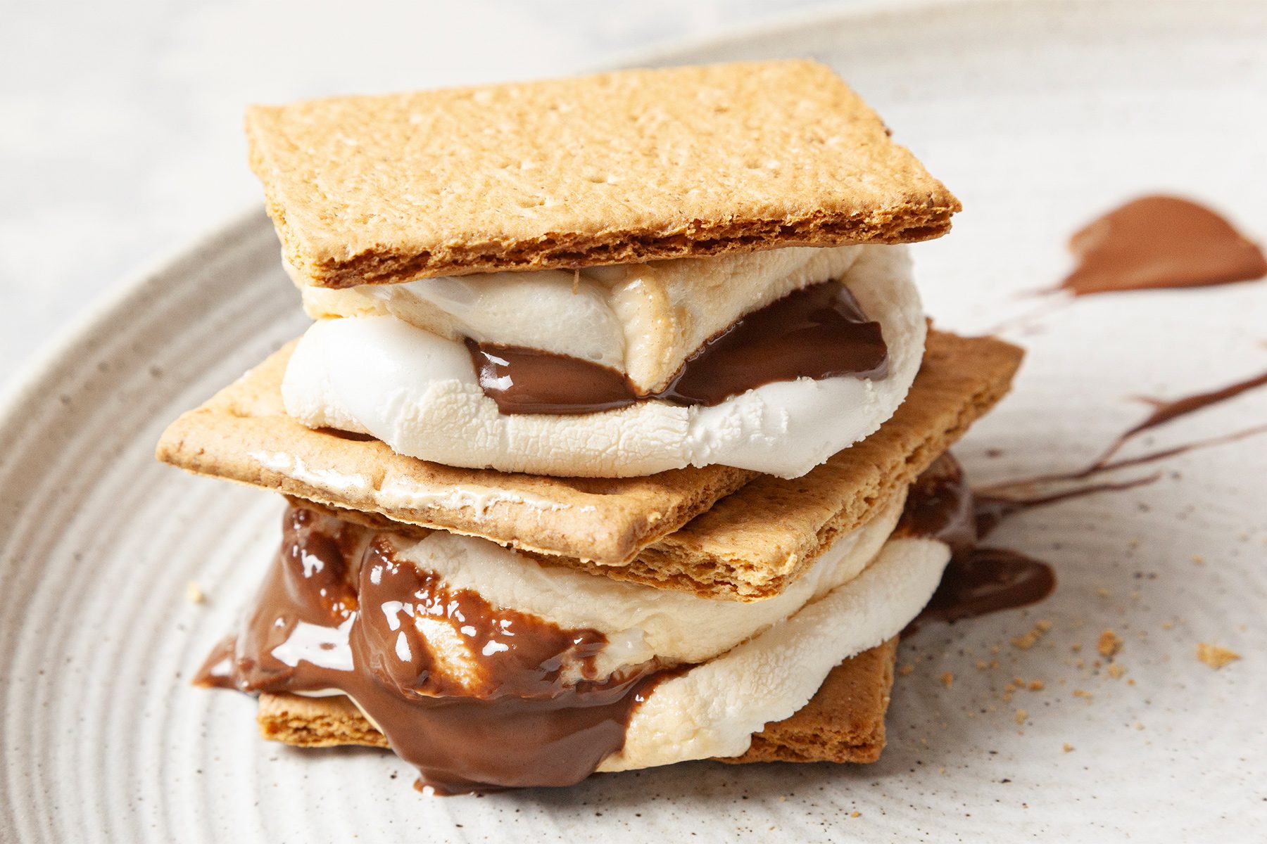 A stack of two s'mores with melted chocolate and marshmallow between graham crackers on a plate.