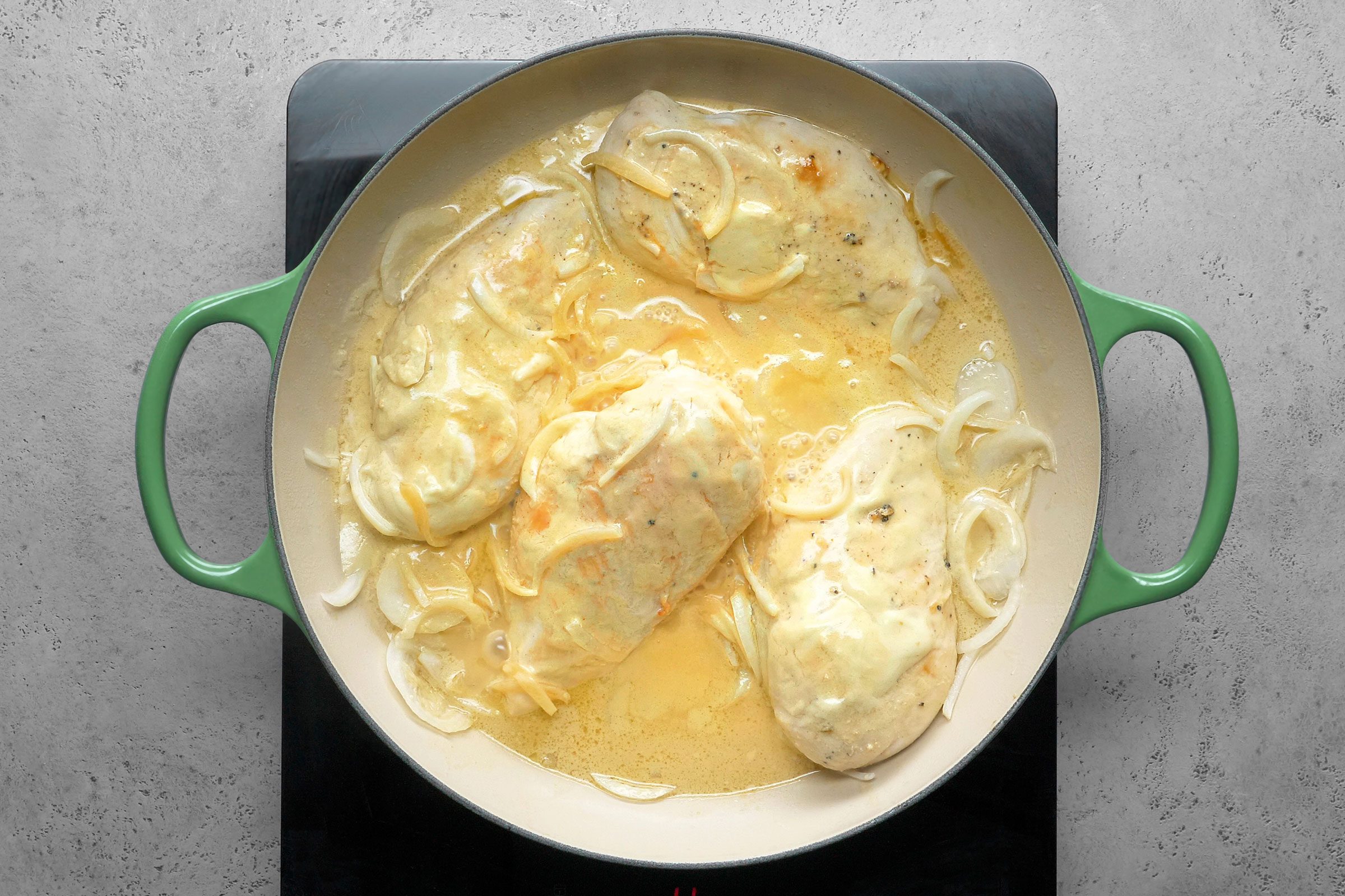 Chicken breasts cooking in a large skillet with onions and cream mixture in it