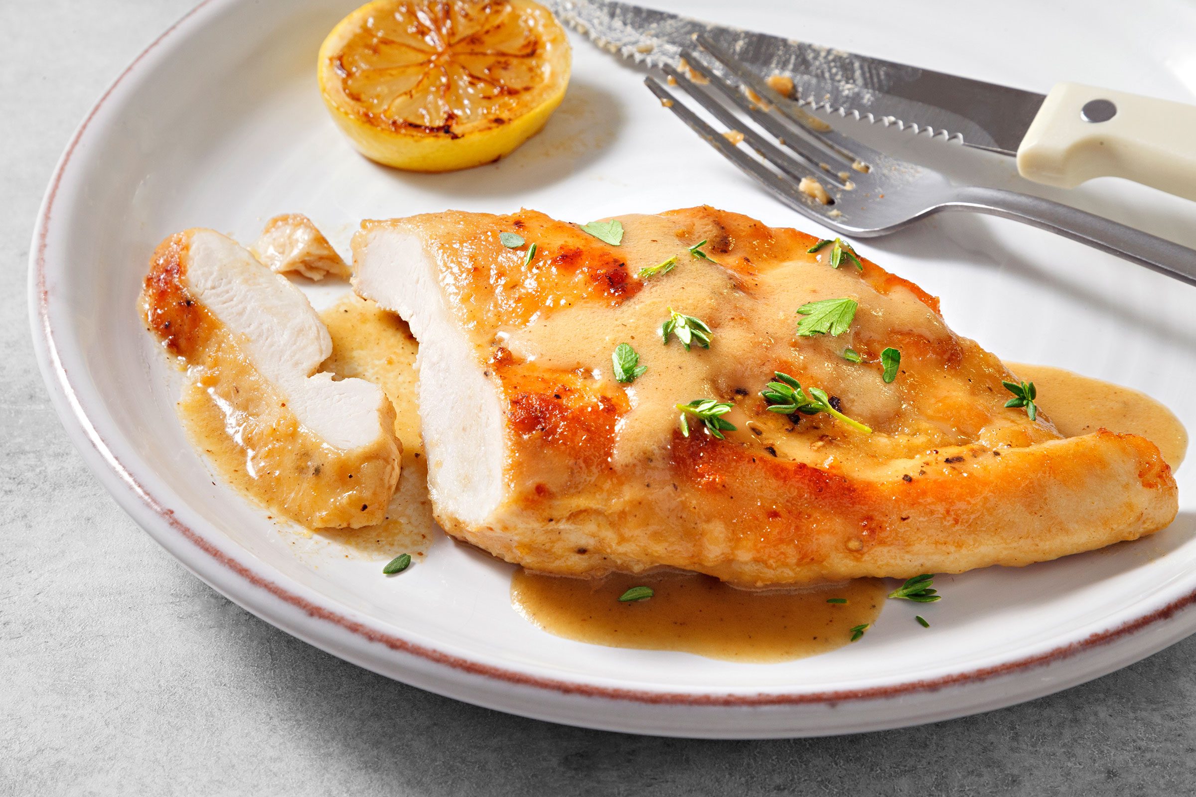 Lemon Chicken served in a white plate and sprinkled with some parsley with lemon on side