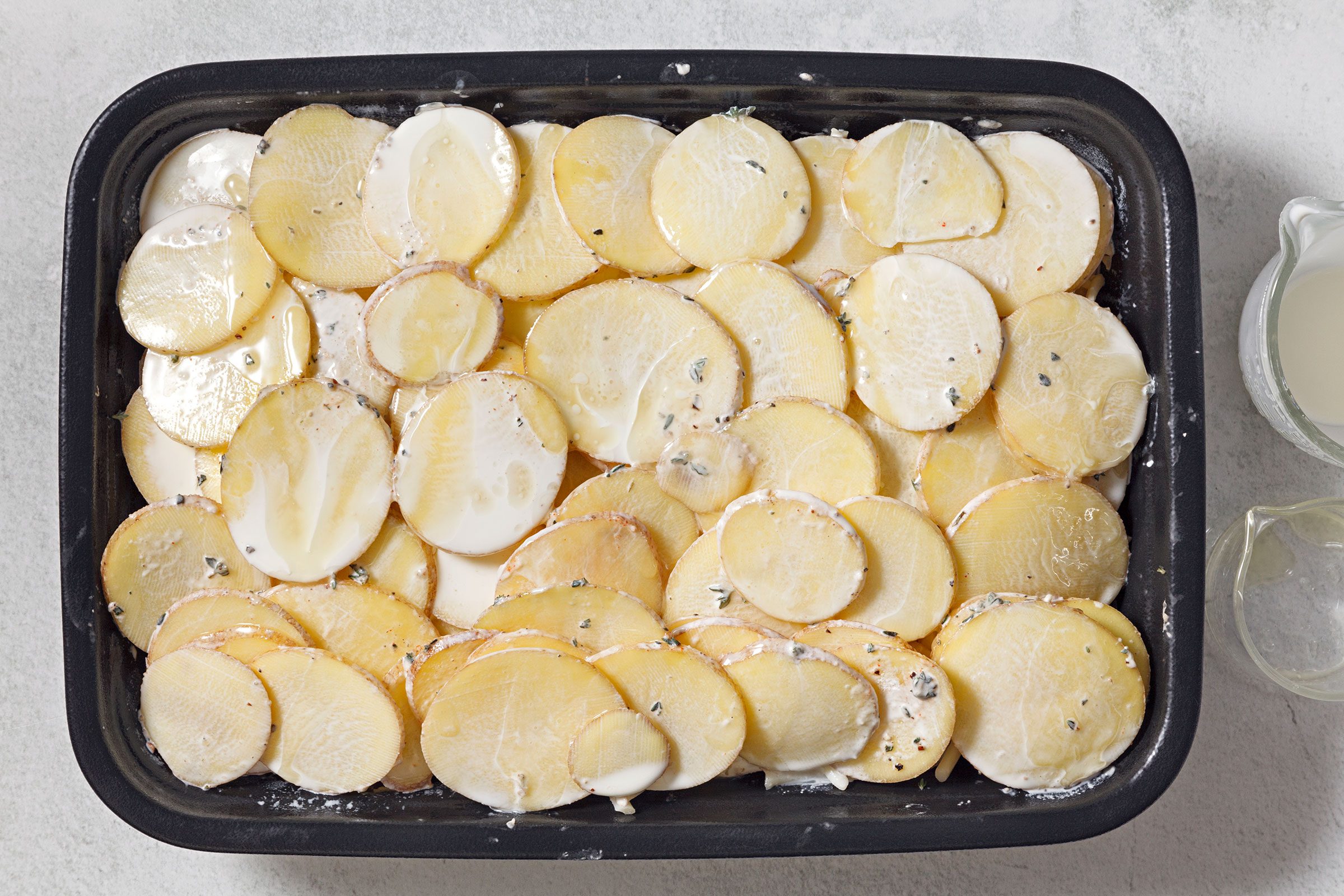 Seasoned potato slices spread on greased baking dish 