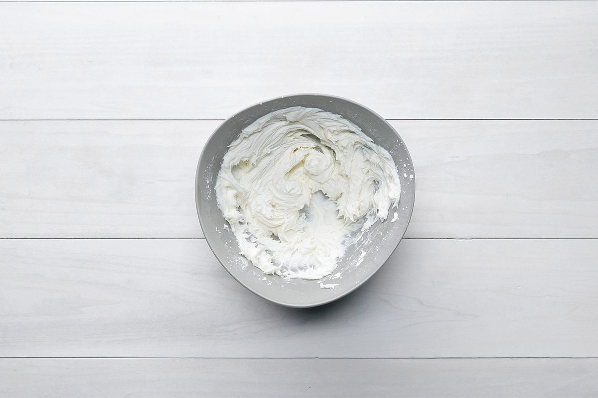 A bowl of whipped cream on a white wooden surface.