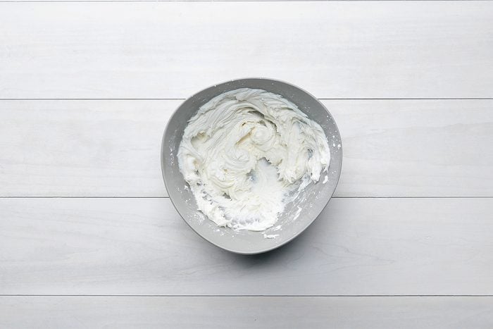 A bowl of whipped cream on a white wooden surface.