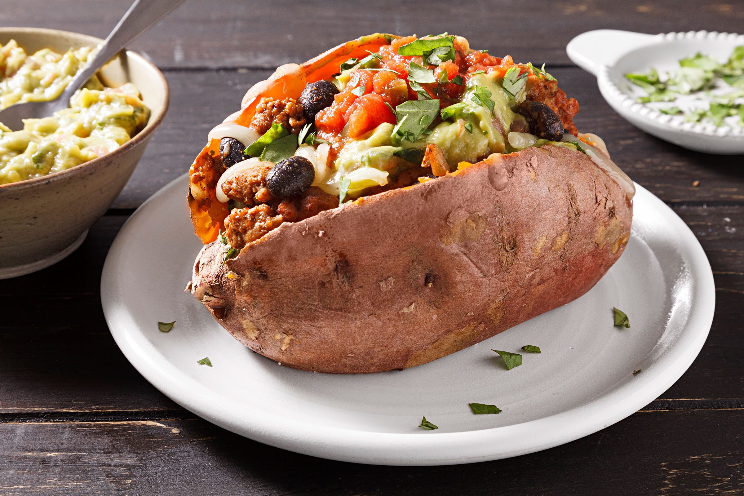 Stuffed Sweet Potatoes served in a plate with guacamole, salsa and cilantro