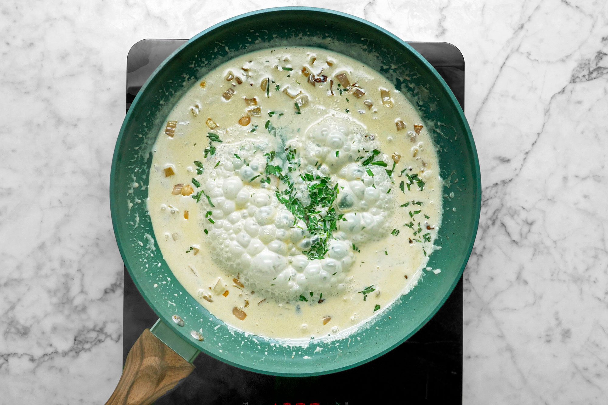 Overhead shot of add shallot to same pan; cook and stir over medium heat until tender; add cream; stirring to loosen browned bits from pan; Increase heat to medium-high; cook until slightly thickened; stir in 2 teaspoons tarragon; lemon juice and remaining salt; induction; marble surface