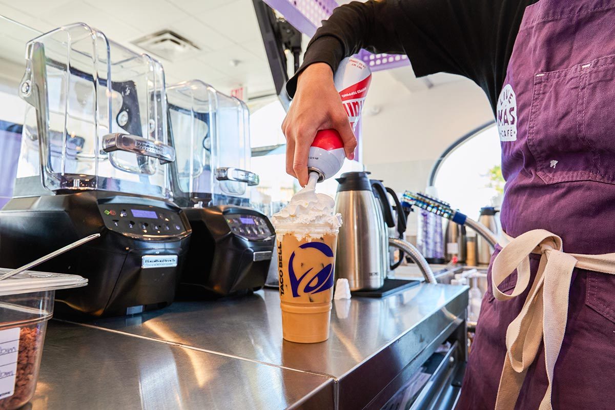 A Live Mas Cafe Barista adds whipped cream to a frappe drink behind the counter