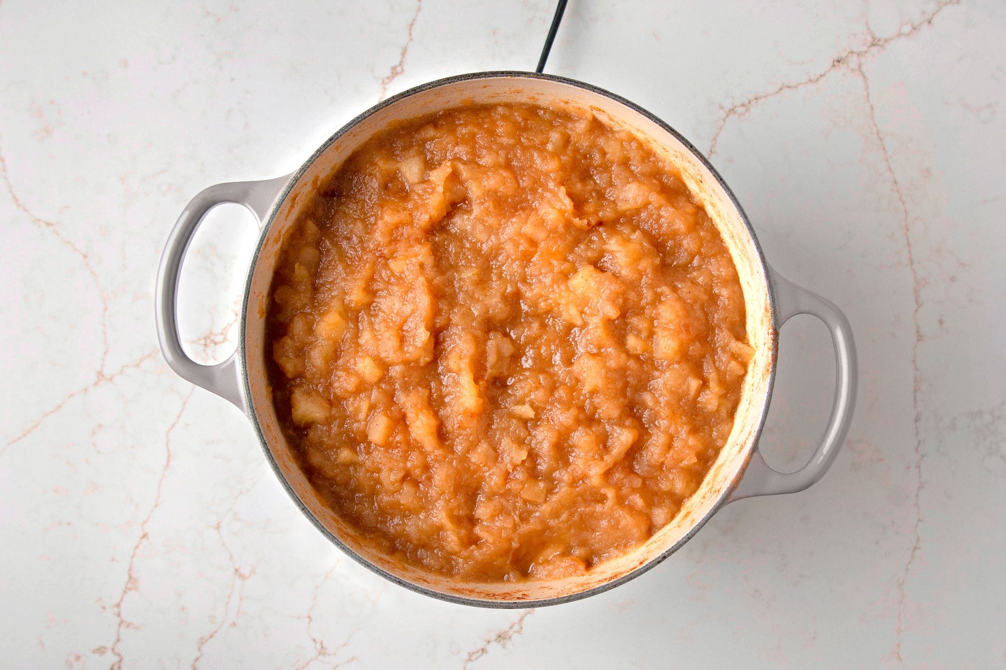 Overhead shot of a pot of applesauce sitting on a marble countertop