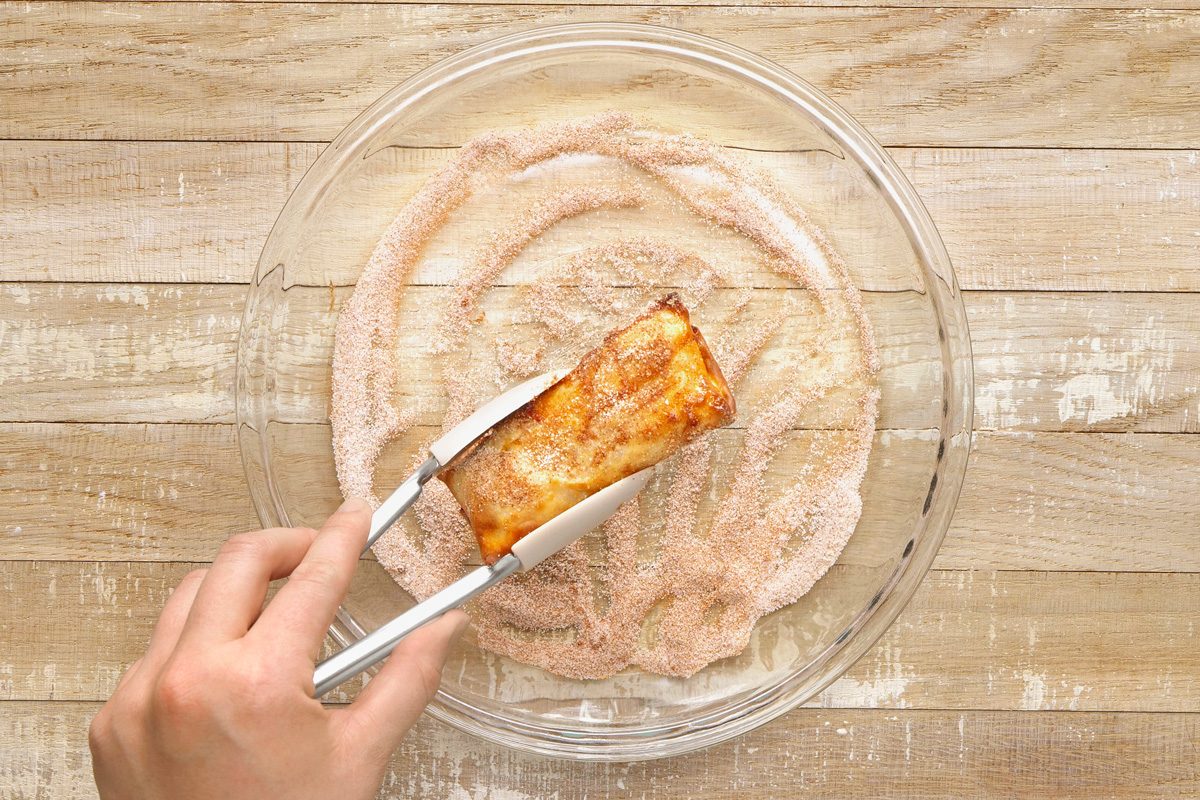 egg rolls being rolled in the cinnamon-sugar mixture in a bowl