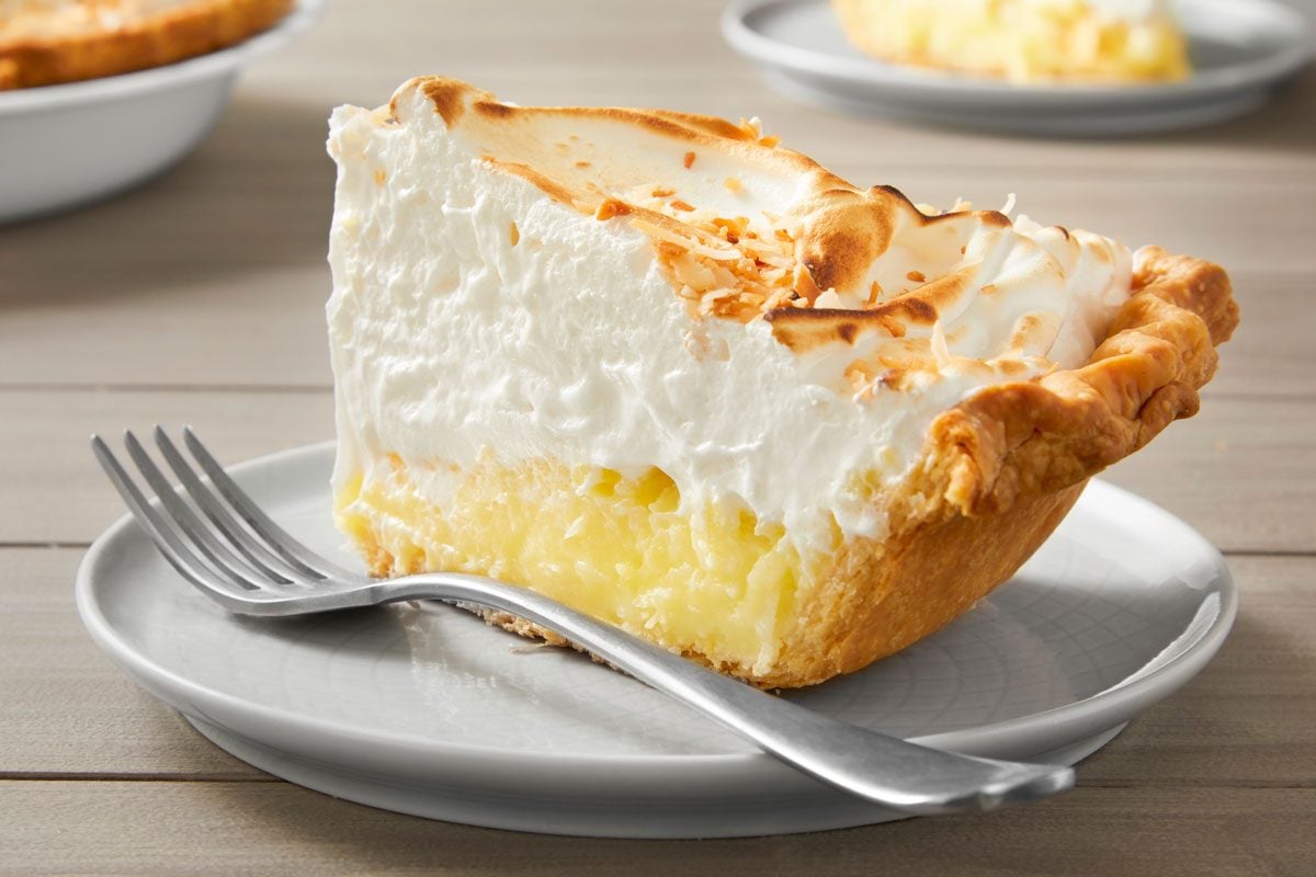 Table view shot of Favorite Coconut Meringue Pie; in a pie plate; cut slice and serve on small plate; with fork; wooden surface;