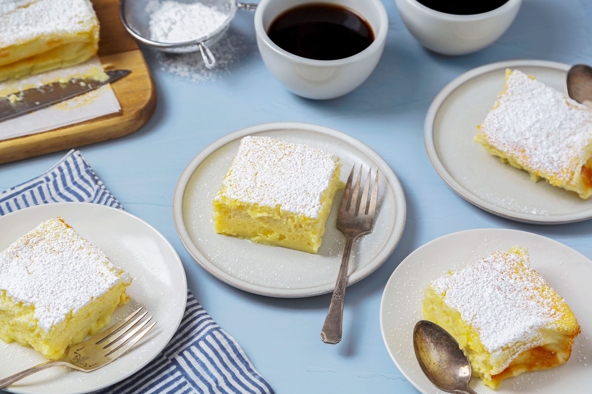 Four custard cakes served on individual white plates, dusted generously with powdered sugar
